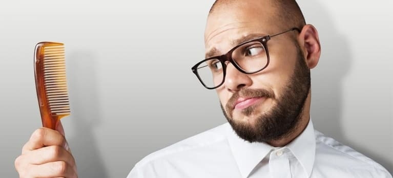 homem calvo olhando para um pente tentando entender a queda de cabelo masculina